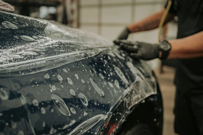 Close-up of hands applying clear paint protection film to a vehicle